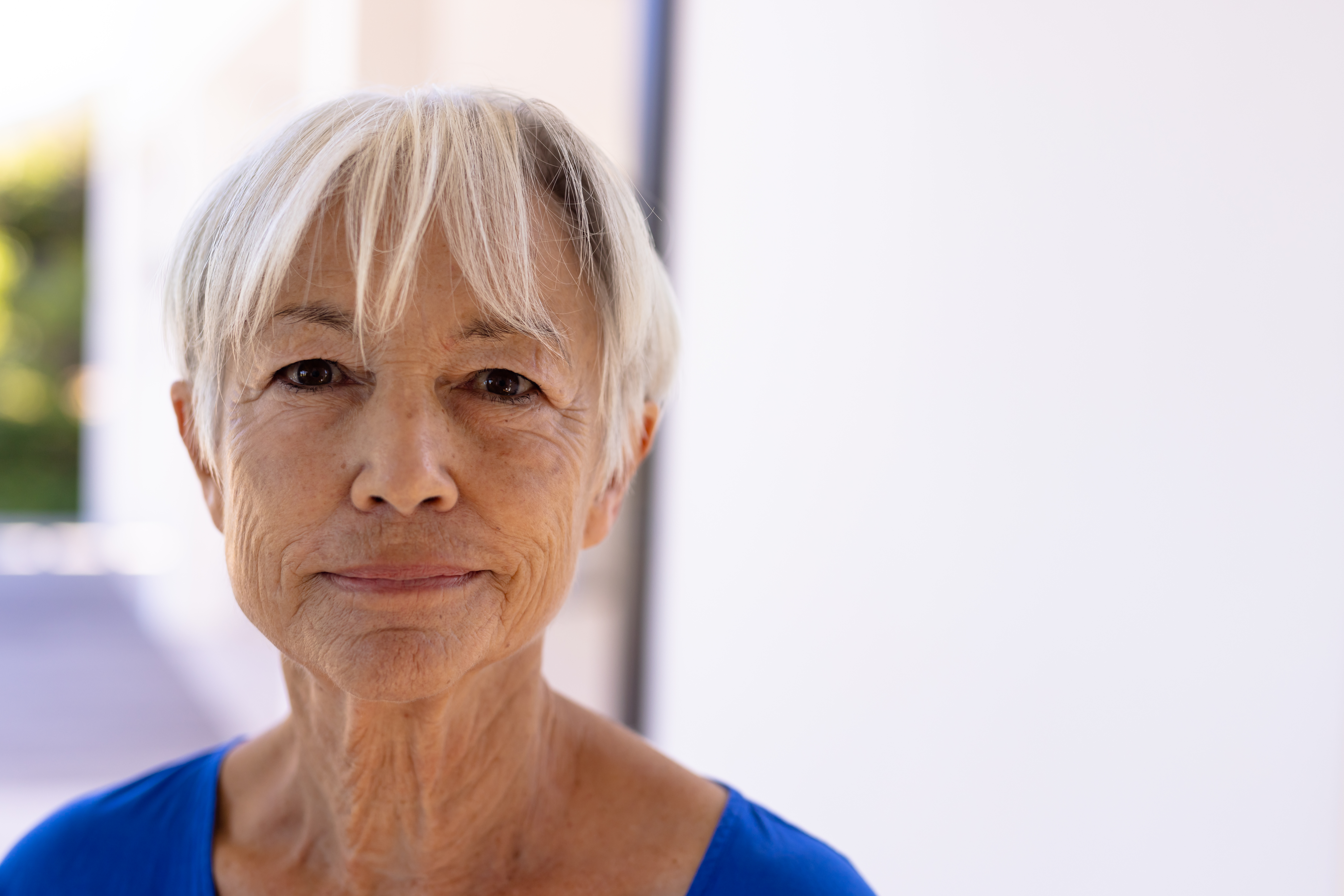 Home close up portrait of smiling asian senior woman with short hair against white wall in nursing home. copy space, wrinkles, unaltered, support, assisted living and retirement concept.