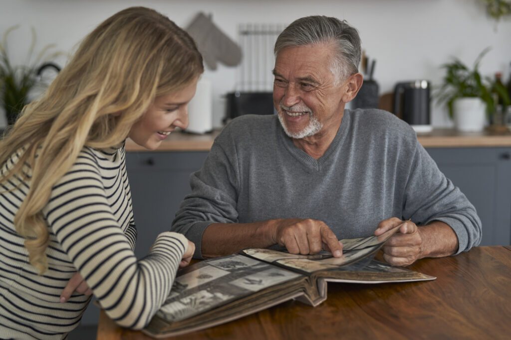 senior man meeting with adult daughter and looking at old pictures in album